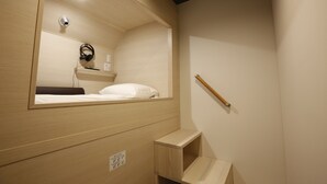 Un dormitorio pequeño con cama, mesita de noche, espejo y una pequeña estantería.