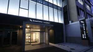 Entrada de un hotel con puerta de cristal, un letrero que dice "Grand Cabin" y un pequeño espacio exterior con un felpudo.