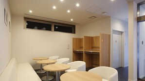 Un área de espera moderna con un banco, cuatro mesas redondas y sillas blancas.