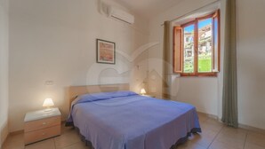 Un dormitori amb llit, taulella de nit, làmpada, aparell d'aire condicionat, finestra amb cortines i una fotografia emmarcada a la paret.