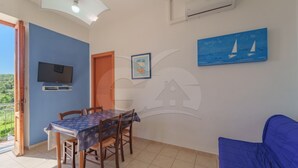 Una habitació amb taula de menjador, cadires, televisió, un quadre i un sofà blau.