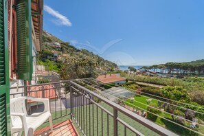 A balcony with a view of a coastal area, including a beach and a hilly landscape.