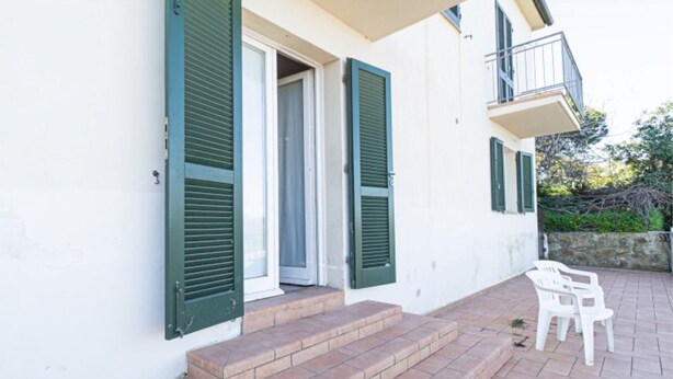 A building with green shutters, a balcony, and a small outdoor seating area. - Two-room apartment with sea view near the famous Sansone beach (Portoferraio)