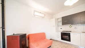 A kitchen with white cabinets, a stove, and a dishwasher. There is a red cabinet and a chair in the corner. - Two-room apartment with sea view near the famous Sansone beach (Portoferraio)