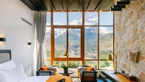 A bedroom with a large window, a bed, a seating area, and a stone wall. - Shinta Mani Mustang (Jomsom)
