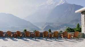 A terrace with wooden chairs and tables overlooking a mountainous landscape. - Shinta Mani Mustang (Jomsom)