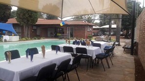 Un área de comedor al aire libre con mesas y sillas, una piscina y sombrillas que dan sombra.