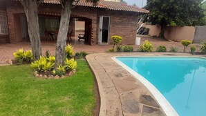 Une piscine bordée de pierres, une pelouse et une maison en briques avec un toit en tuiles.