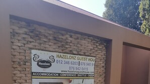 Un mur de briques sur lequel est apposée une enseigne publicitaire pour la maison d’hôtes Hazelonz, qui propose des hébergements, des salles de conférence, un service de navette et des prestations de restauration.