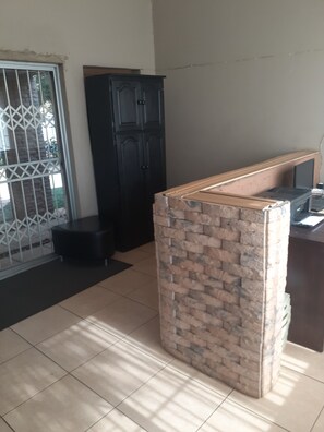 Una habitación con piso de baldosas, un armario negro, un taburete pequeño negro y una encimera de madera con una computadora.