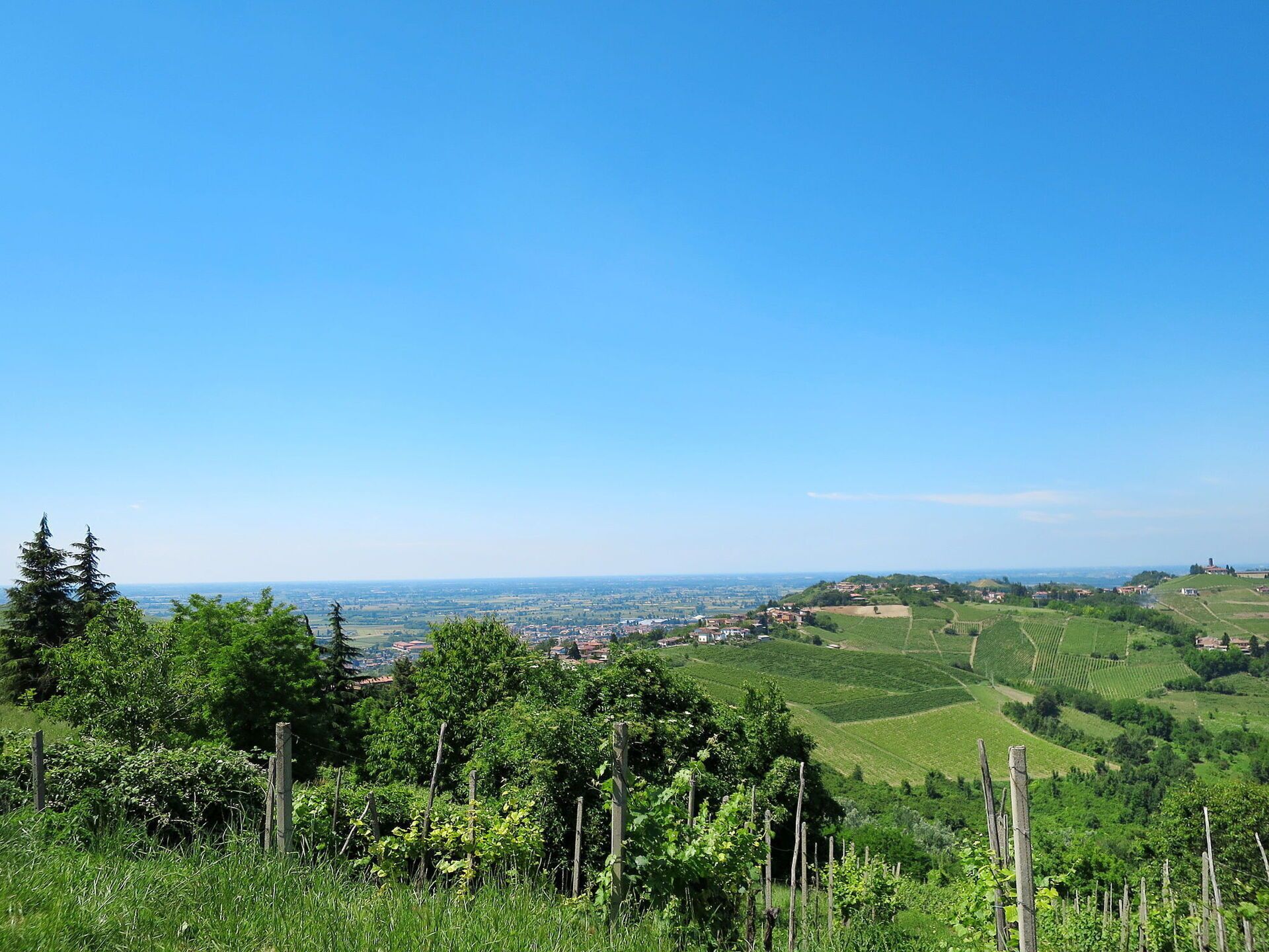 Paesaggio rurale con vigneti, un piccolo borgo e un cielo azzurro limpido.