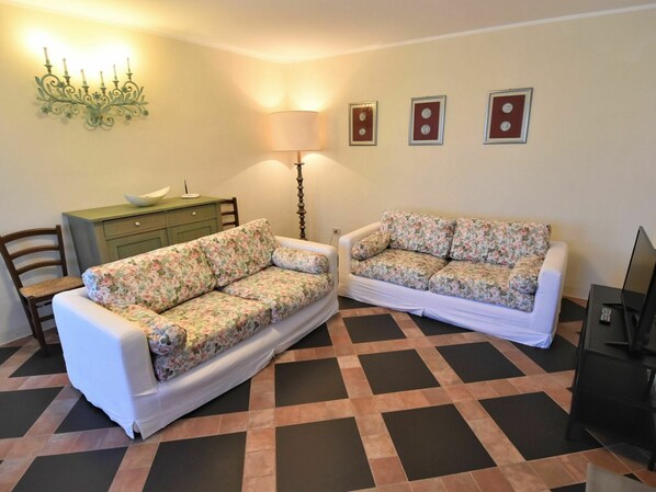 A living room with two floral-patterned sofas, a wooden cabinet, a floor lamp, and a television.