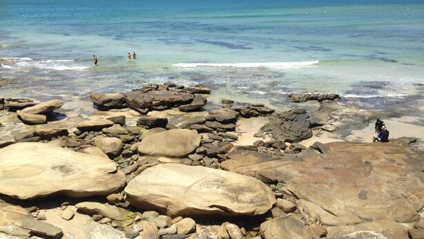 A rocky beach with clear water and a boat in the distance. - XYL seaside home stay (Caloundra)