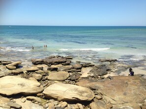 A rocky beach with clear water and a boat in the distance. - XYL seaside home stay (Caloundra)