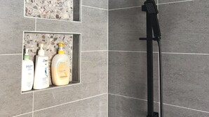 A shower area with a square showerhead, a handheld showerhead, and a shelf with toiletries. - XYL seaside home stay (Caloundra)