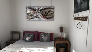 A bedroom with a bed, pillows, a wall-mounted abstract painting, a bedside lamp, and a hookboard. - XYL seaside home stay (Caloundra)