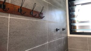 A bathroom with a wooden towel rack, a glass shower enclosure, and tiled walls. - XYL seaside home stay (Caloundra)