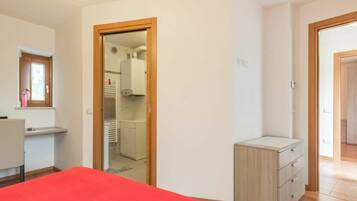 Ein Schlafzimmer mit einem roten Bett, einer Holzkommode und einem Kleiderschrank mit Spiegel und Fenster.