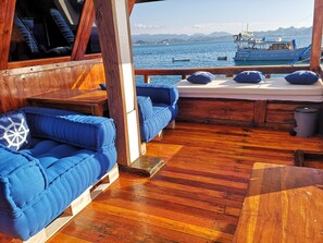 A wooden deck with blue cushioned seating and a view of the sea. - Sumba Ocean Phinisi (Labuan Bajo)