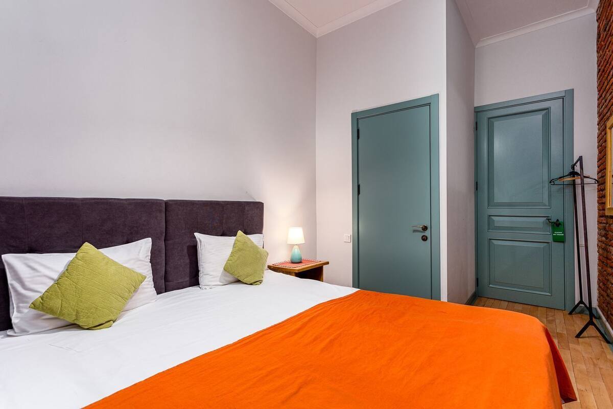 A bedroom with a bed, pillows, a nightstand, a lamp, and two doors.