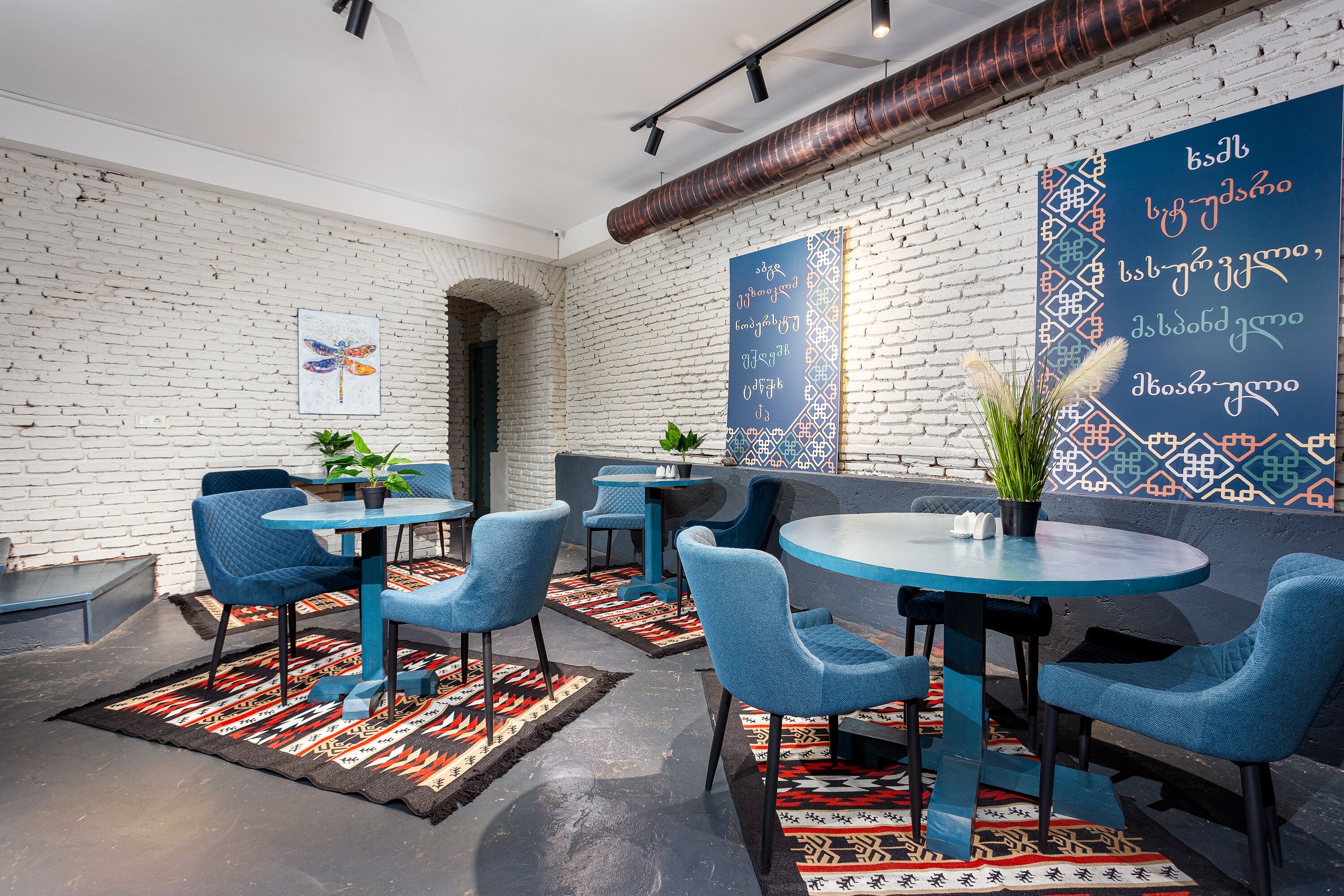 Un intérieur moderne avec des chaises et des tables bleues, un mur en briques et des panneaux décoratifs ornés de texte.