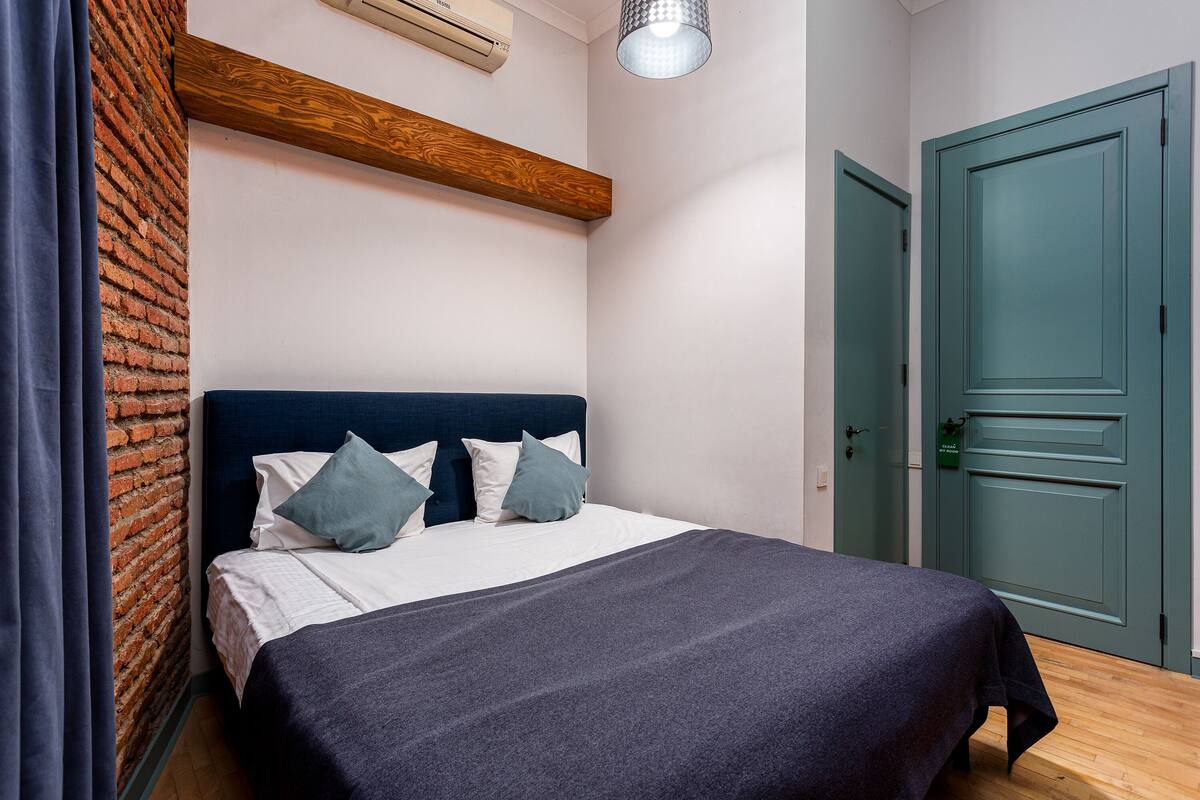 A bedroom with a bed, a wooden beam, a brick wall, and a green door.