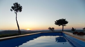 Piscina con vistas al atardecer, rodeada de árboles y un paisaje lejano.