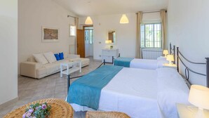 Un dormitorio amplio con dos camas, una zona de estar con sofá, un aparador y un ventanal que proporciona luz natural.