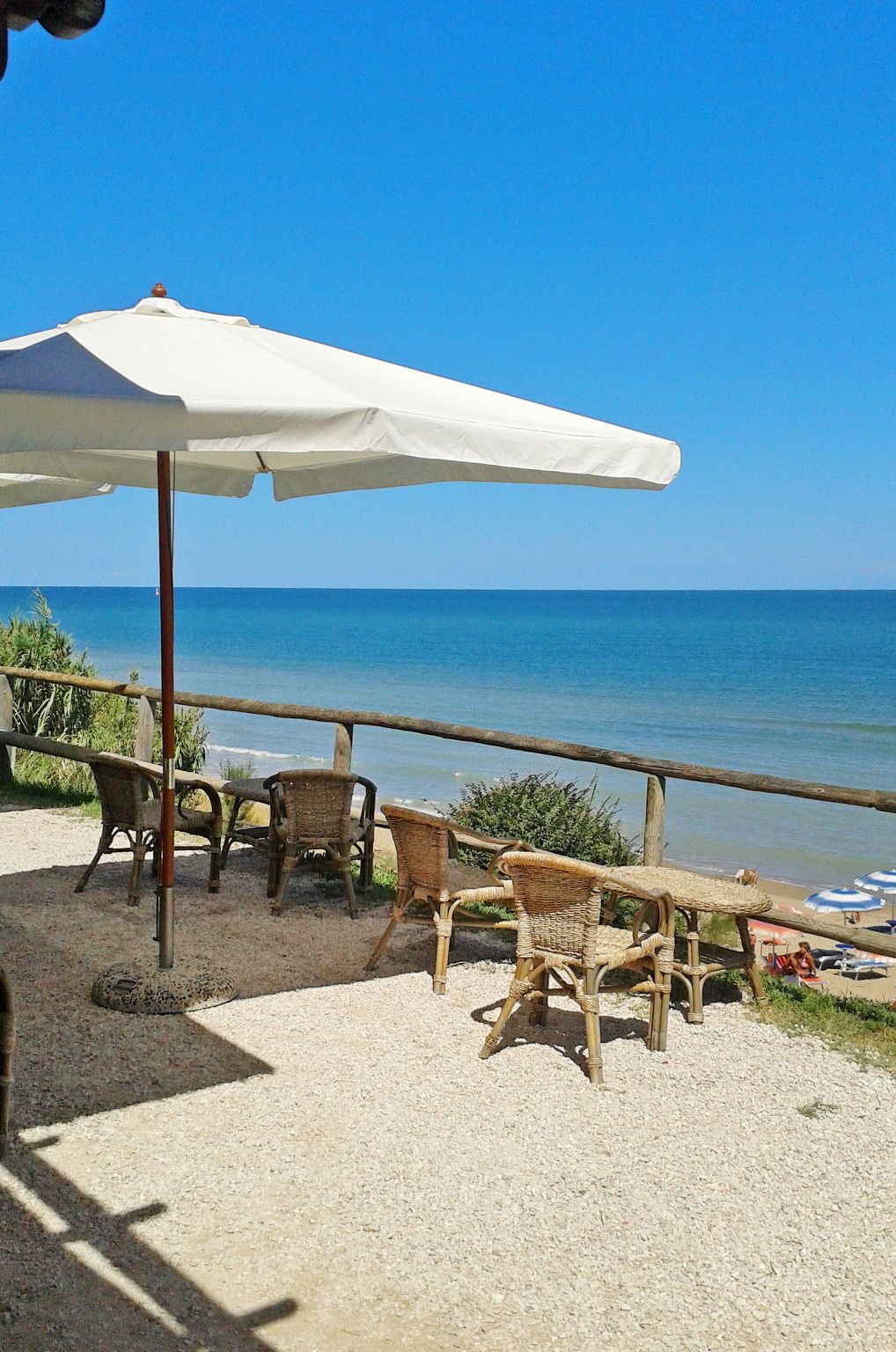 Un espace aménagé avec des chaises en osier et un parasol blanc, situé en bord de plage et offrant une vue sur la mer.