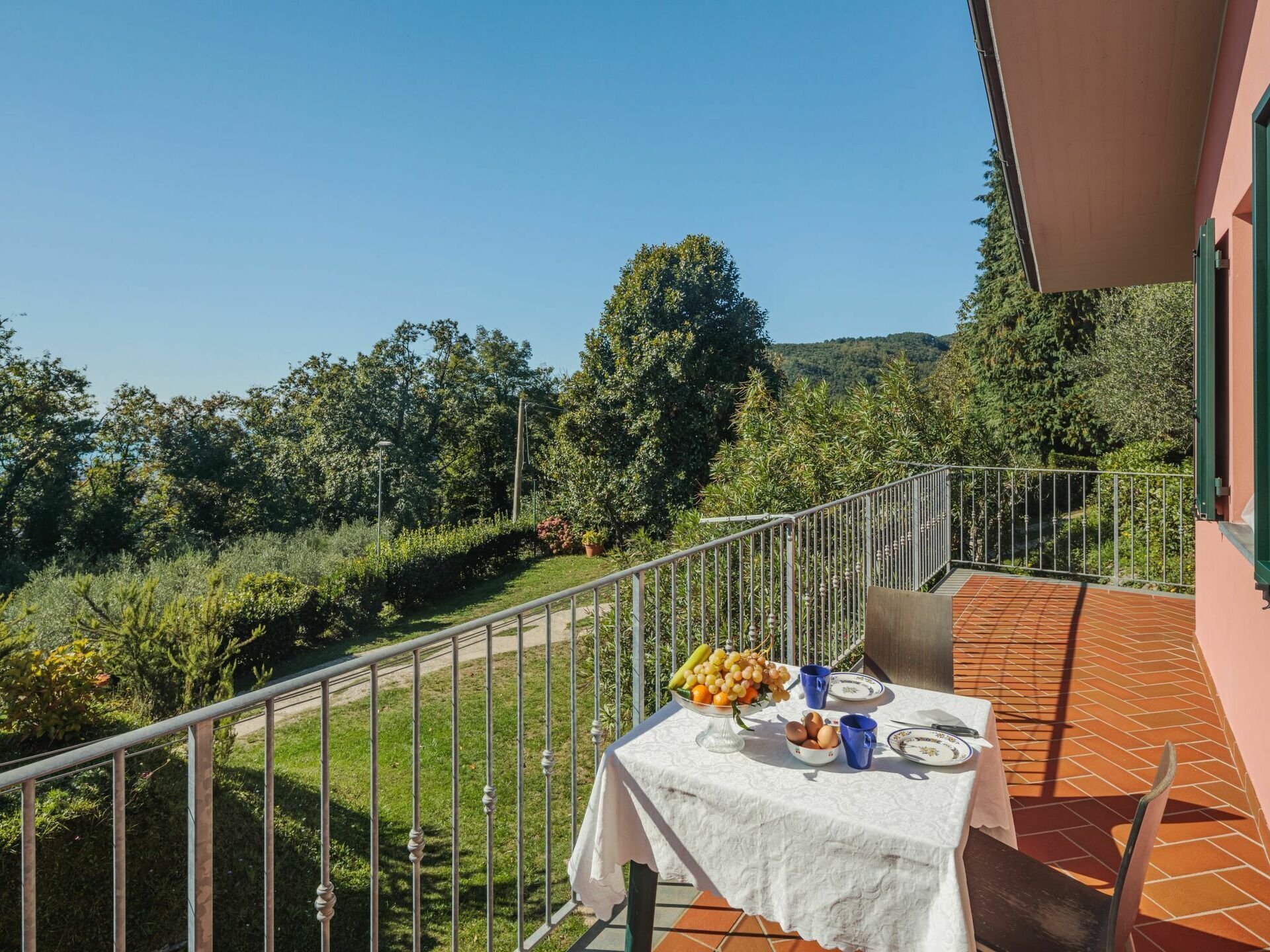 Eine Terrasse mit Tisch für zwei Personen, mit Blick auf einen üppigen Garten und eine Hügelkuppe.