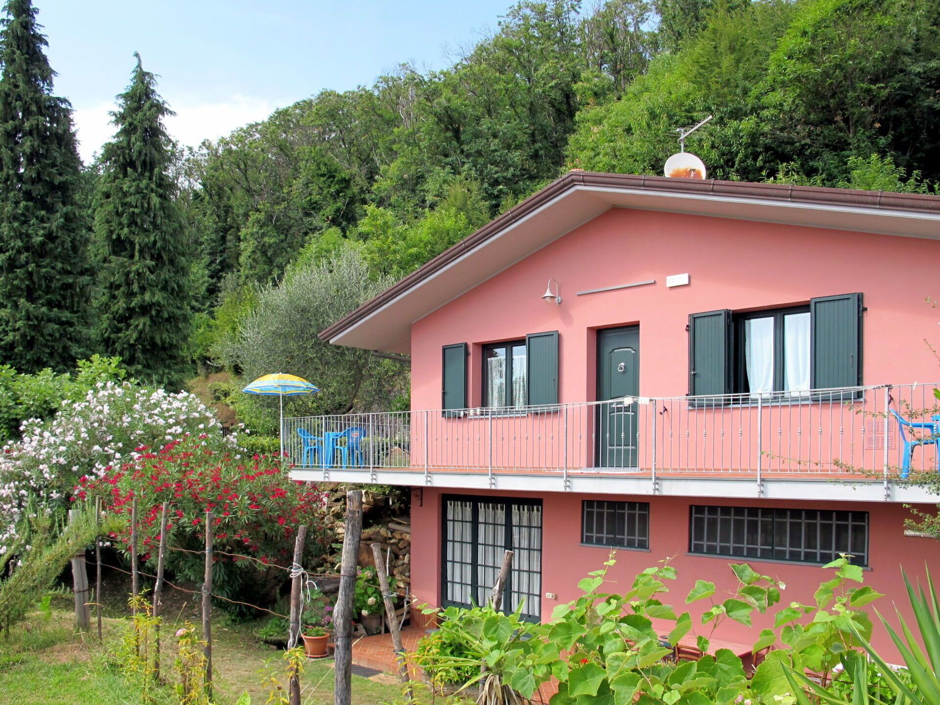 A pink house with a balcony, surrounded by greenery and trees.