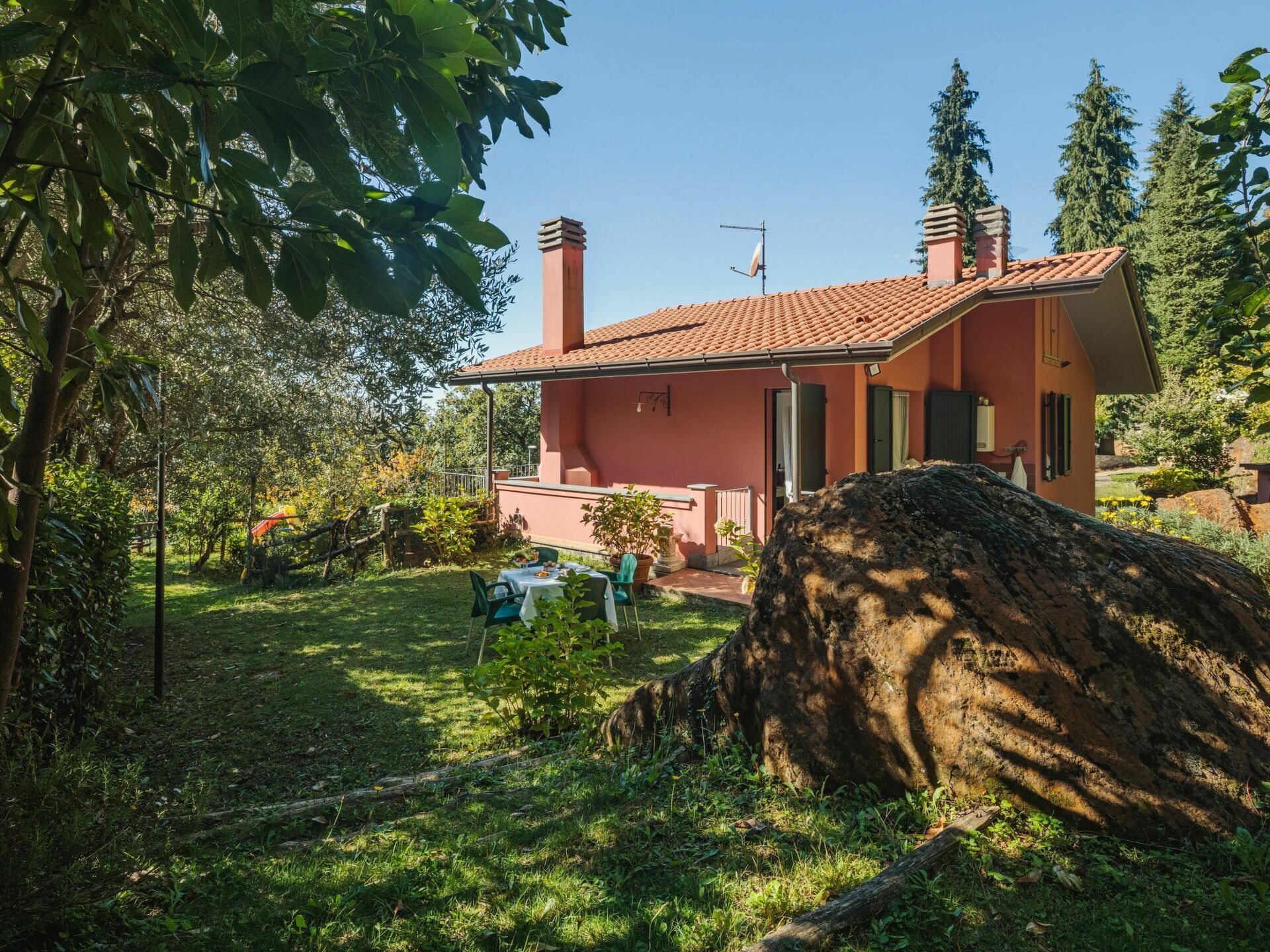 A house with a red-tiled roof, a chimney, and a garden with a table and chairs.