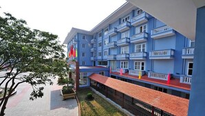 Un hôtel à plusieurs étages doté de balcons, d’un toit recouvert de tuiles rouges et d’une cour aménagée.