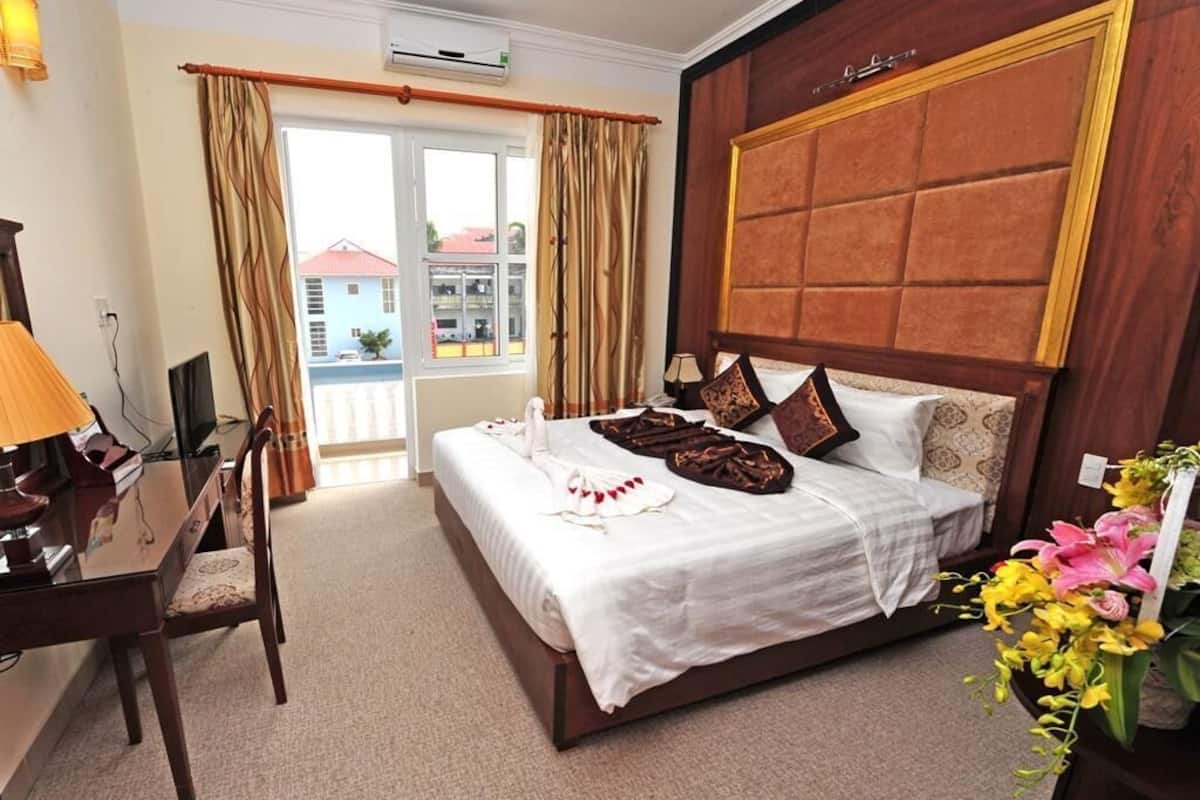 Une chambre d’hôtel avec un grand lit, un bureau avec une lampe et une vue sur l’extérieur par une fenêtre.