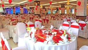 Une salle de banquet avec des tables rondes dressées pour un événement formel, décorée d’éléments rouges et blancs.