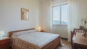 A bedroom with a bed, a nightstand, a table, a chair, a chandelier, a window with curtains, and a radiator. - Cosy apartment for 6 people with WIFI, TV, patio and pets allowed (Montignoso)