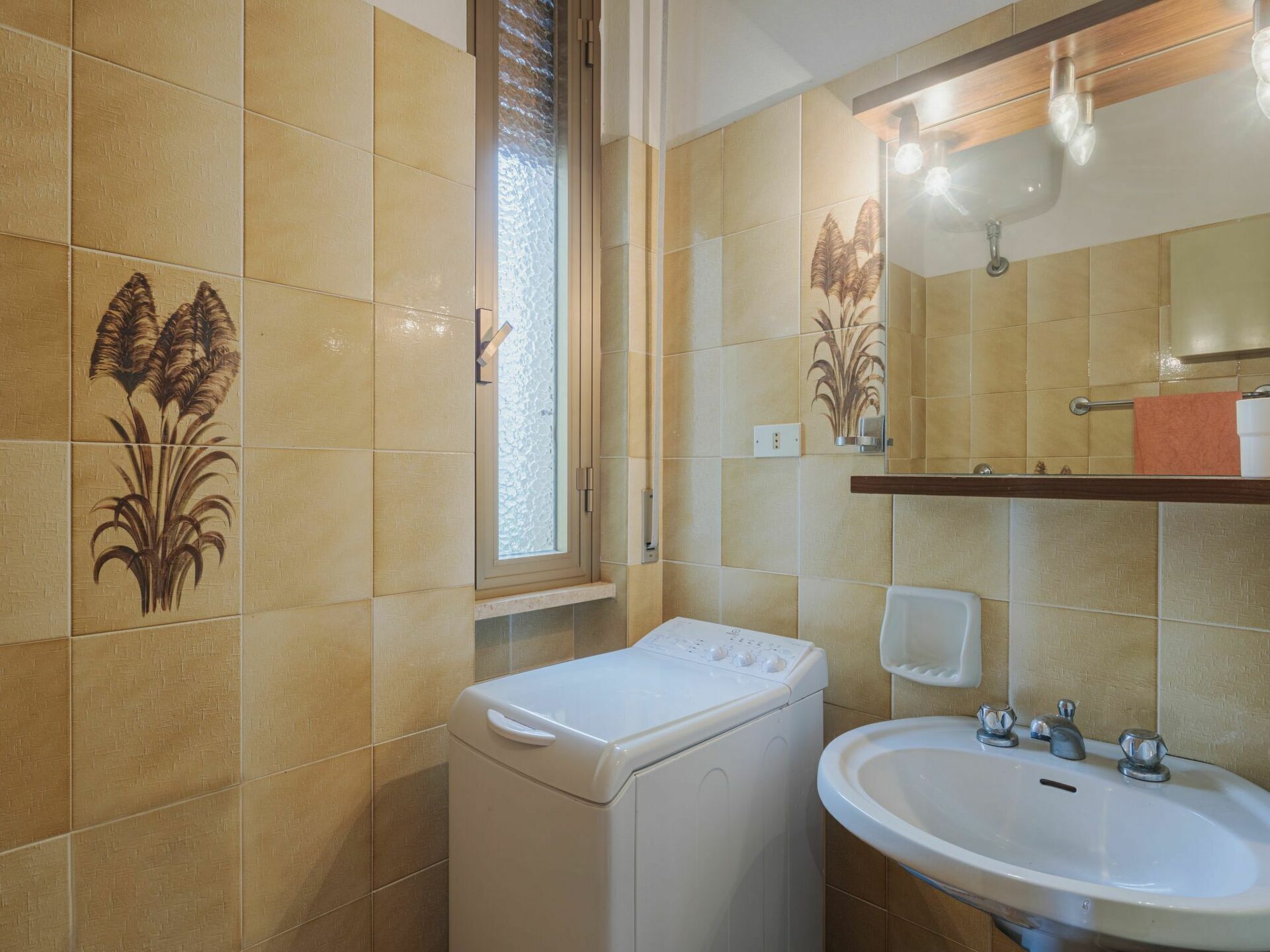 A bathroom with beige tiles, a washing machine, a sink, and a mirror with a towel rack.