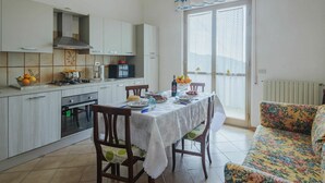 A modern kitchen with white cabinets, a dining table set with plates and glasses, and a sofa with a floral pattern. - Cosy apartment for 6 people with WIFI, TV, patio and pets allowed (Montignoso)