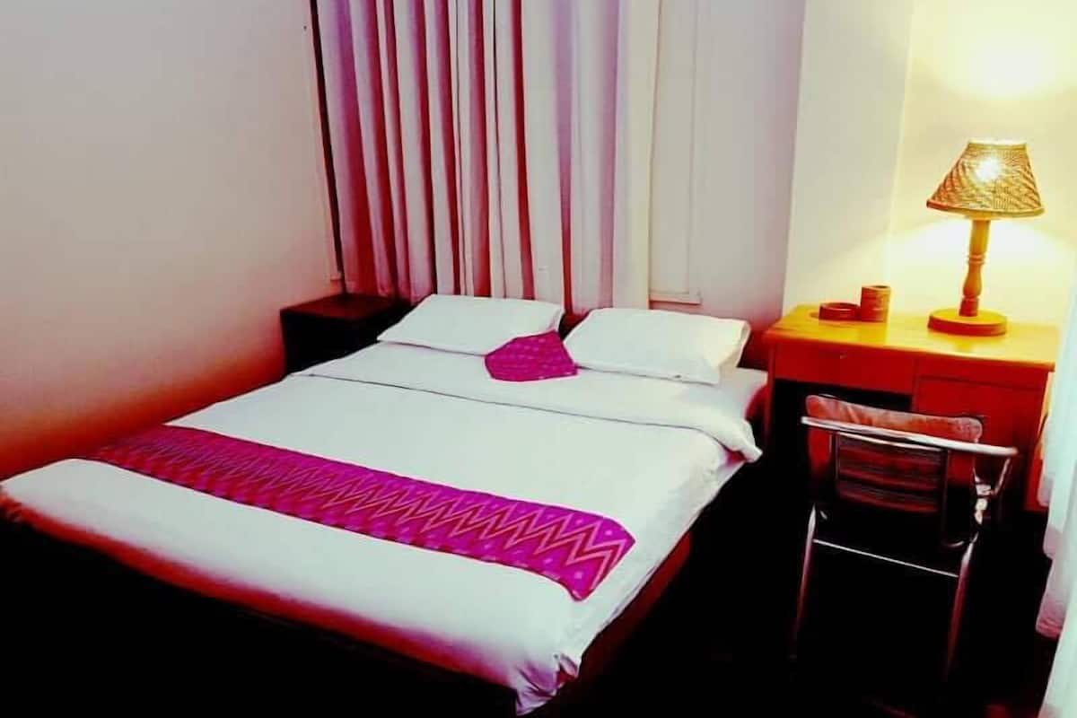 A hotel room with a bed, a desk, a chair, and a lamp.