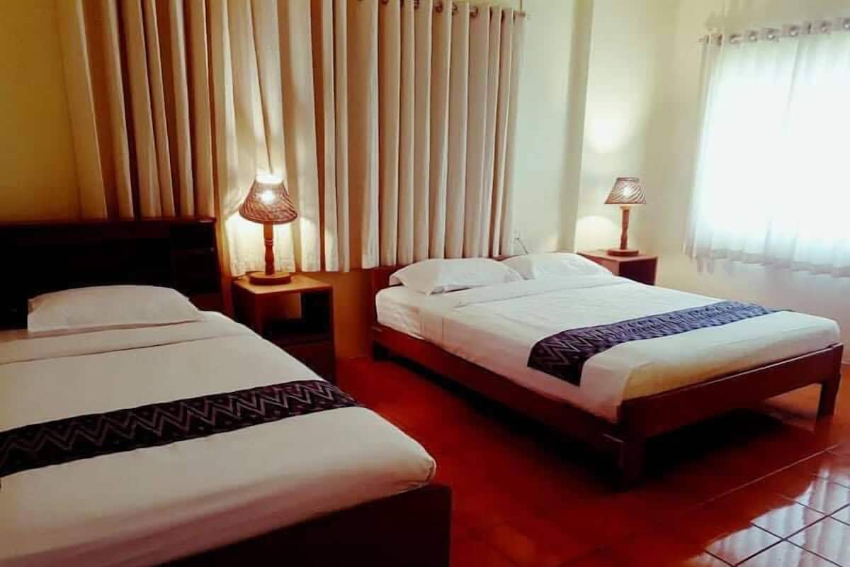 A hotel room with two beds, a wooden floor, and a window with curtains.