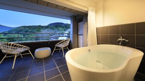 Un bagno moderno con una vasca da bagno grande, due poltrone in vimini e vista su un paesaggio montano.