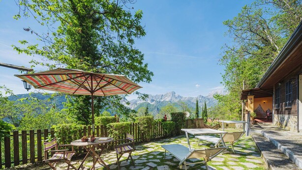 Eine Terrasse mit Tisch, Stühlen und Sonnenschirm, mit Blick auf eine Berglandschaft.