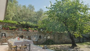 Un patio con una mesa lista para comer, rodeado de muros de piedra y plantas en macetas.