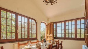 Comedor con una mesa dispuesta para cuatro personas, ventanas grandes y una araña.