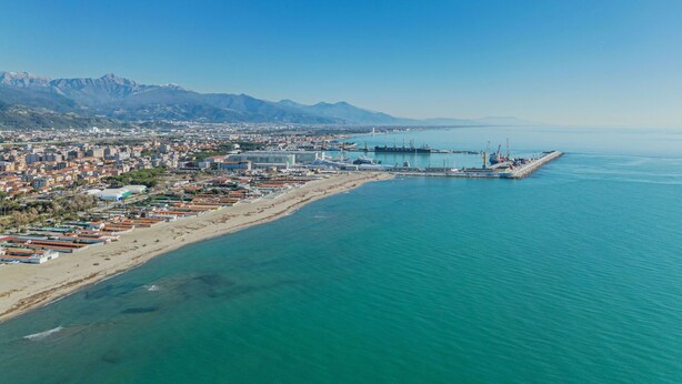 Vista aérea de una ciudad costera con un puerto deportivo, edificios y montañas al fondo.