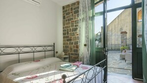A bedroom with a bed, a stone wall, a window with curtains, and an open door leading to a courtyard. - Lovely apartment for 6 guests with private pool, WIFI, A/C, TV, terrace and pets allowed (Lugliano)