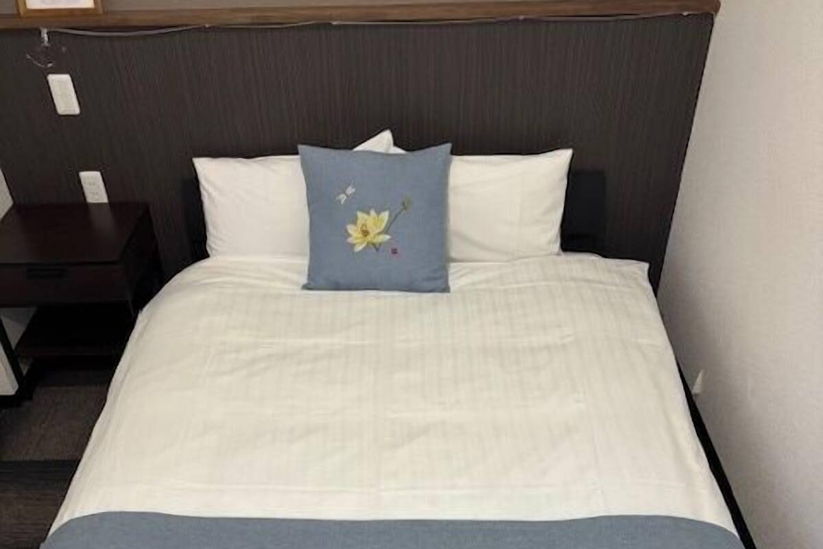 A neatly made bed with white linens, a blue pillow with a floral design, and a blue blanket with a floral pattern.