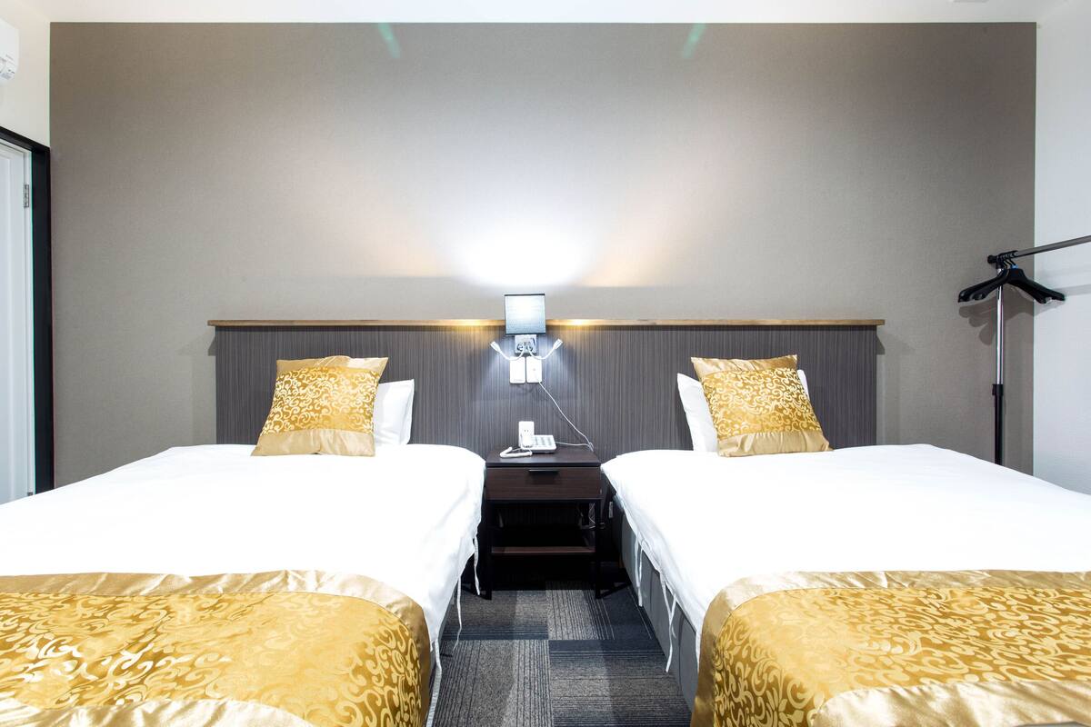 A hotel room with two single beds, a bedside table, a lamp, and a wall-mounted light fixture.