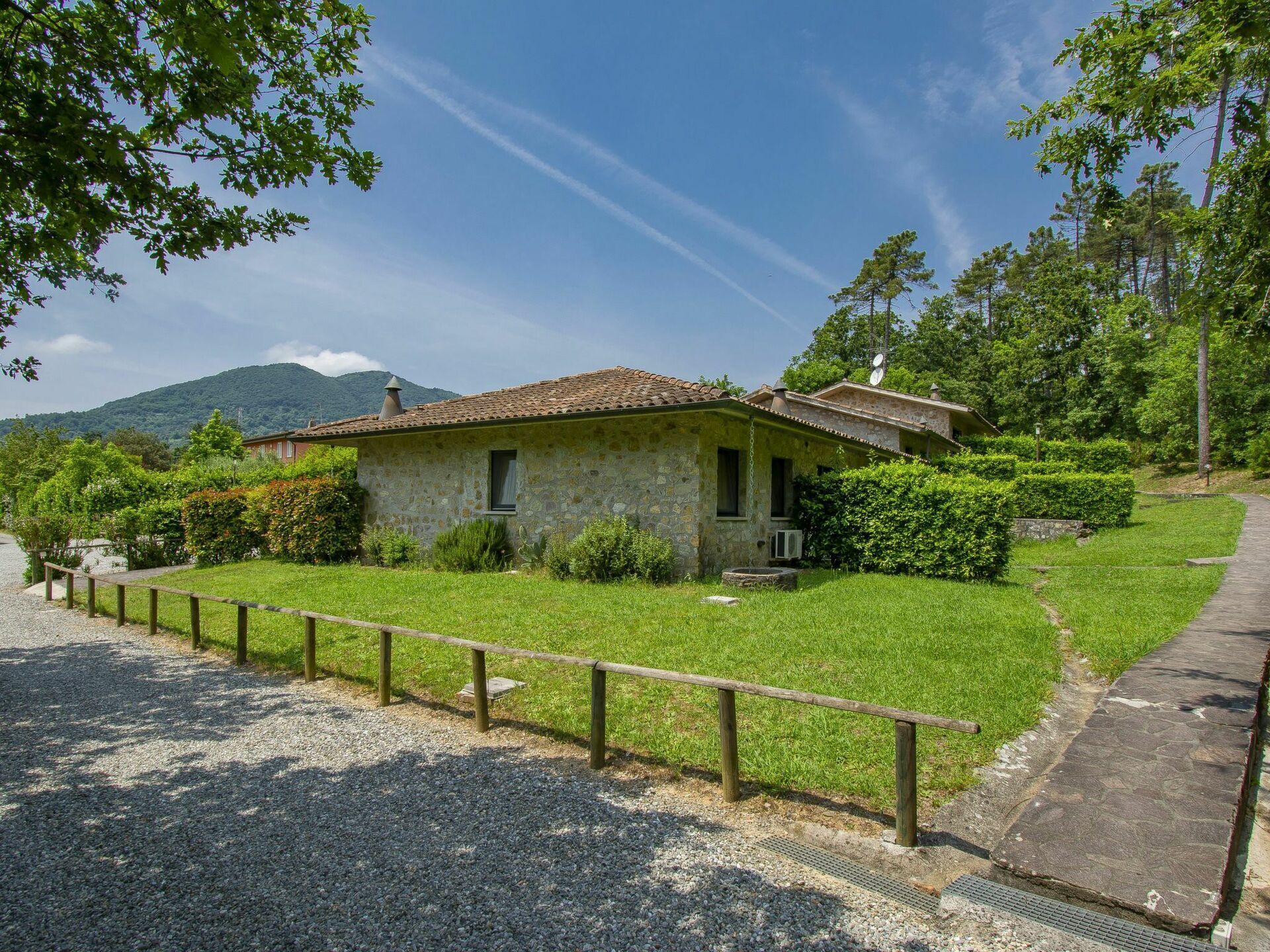 Una casa de piedra con techo de tejas, rodeada por un camino de grava y una cerca de madera.