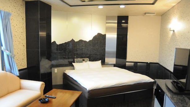 Habitació d'hotel moderna amb llit, sofà, taula petita i televisió.